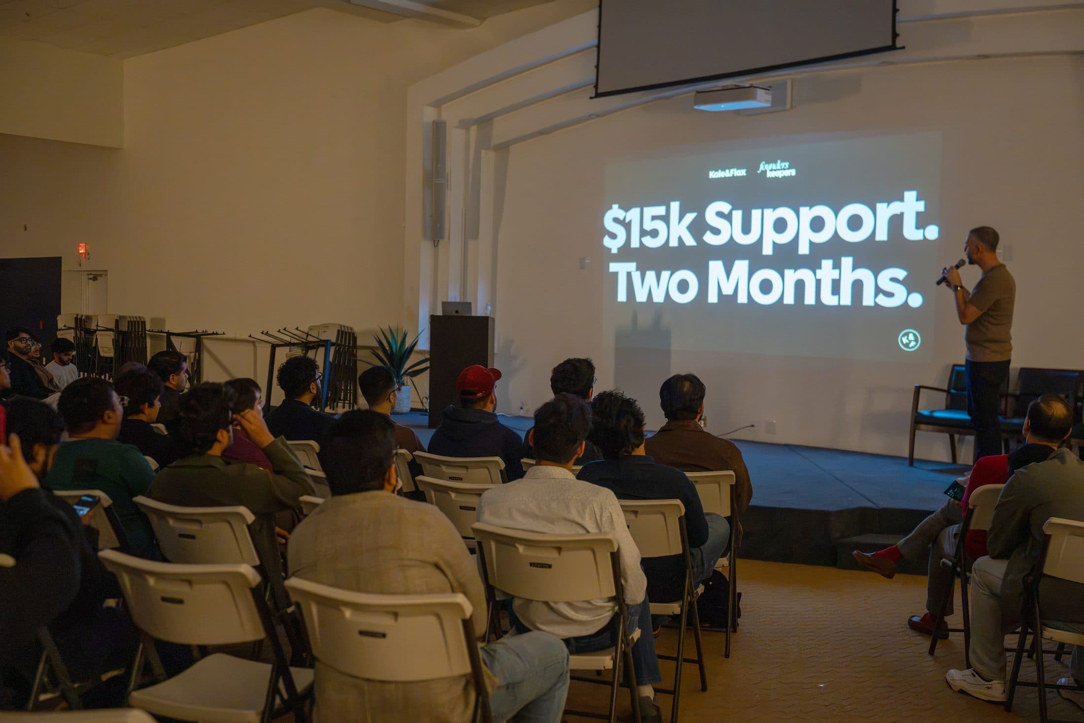 The “$15k Support. Two Months.” slide over a seated audience