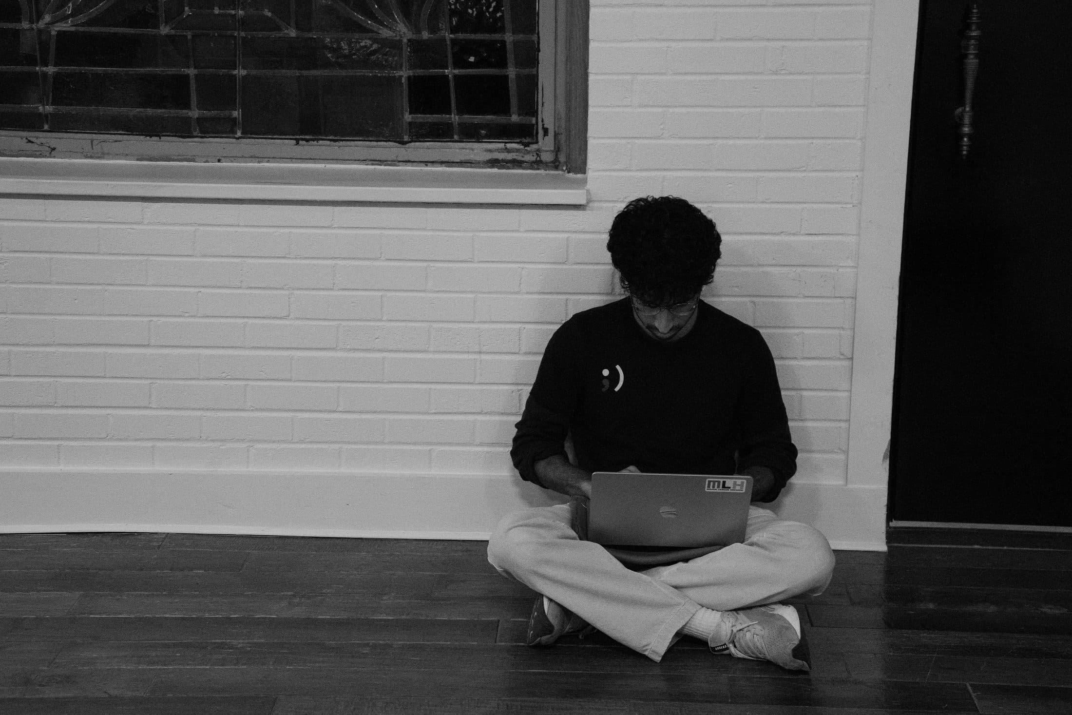 A builder on the floor against the wall, laptop on his knees